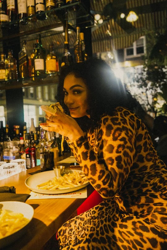 Young woman holding a cheeseburger slyly in front of a dimly lit restaurant bar
