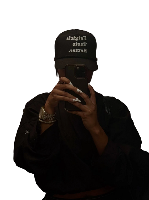 Person wearing a black cap and hoodie with text, holding a phone on a white background